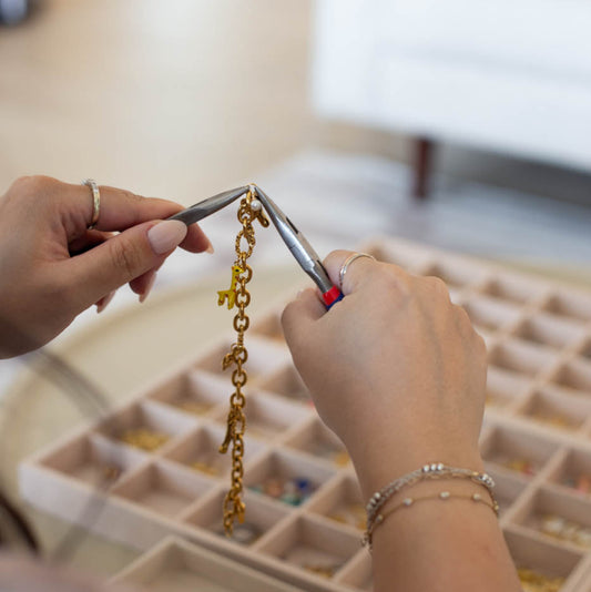 Person working on a gold chain with pliers to assemble charms.