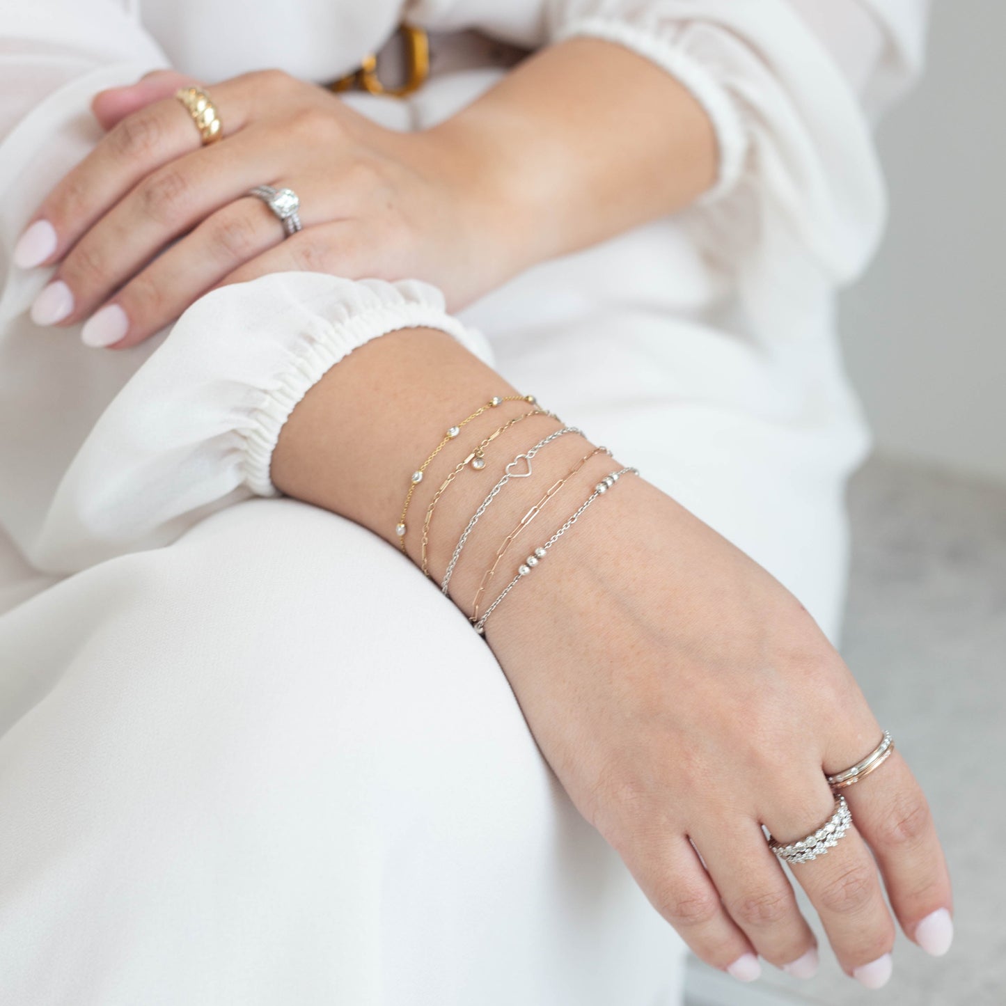 Close-up of a person's wrist with multiple gold bracelets and rings on a neutral background