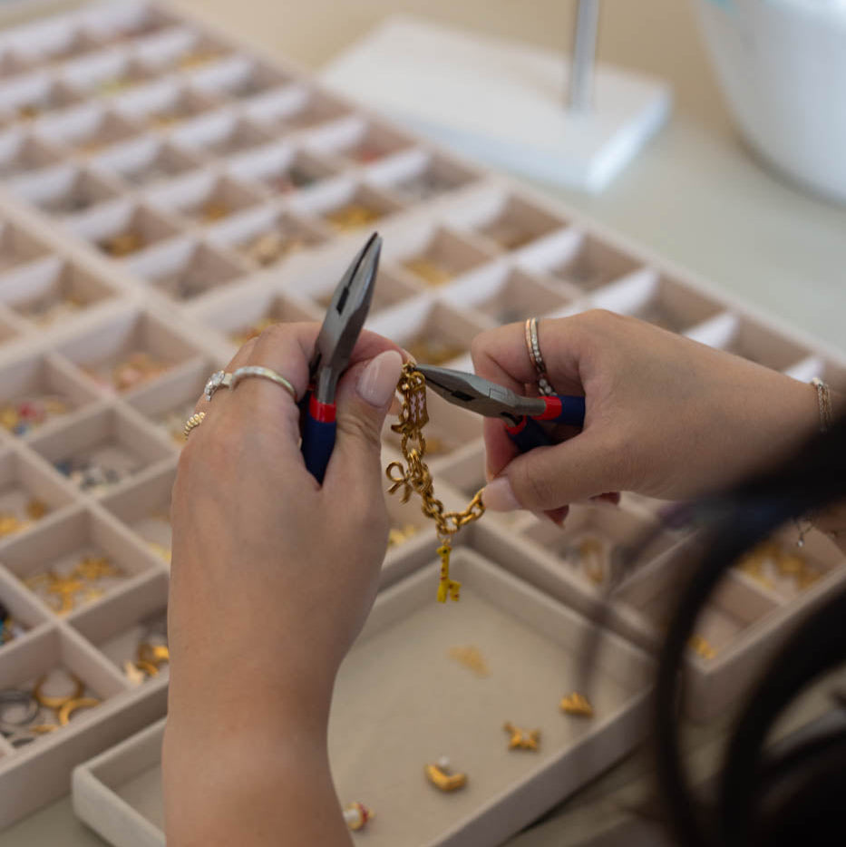 Person working with jewelry on a table with tools and materials.