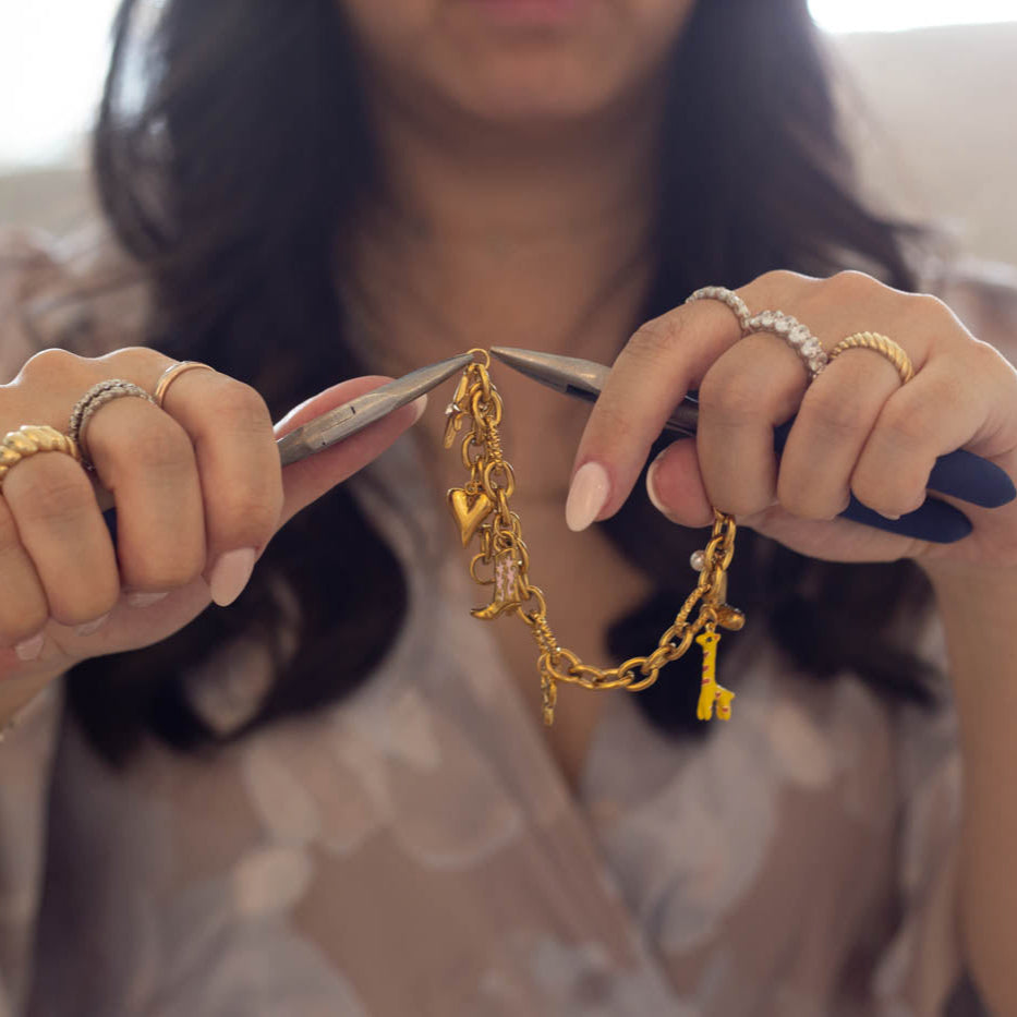 Person holding a gold chain with scissors, wearing multiple rings and bracelets.