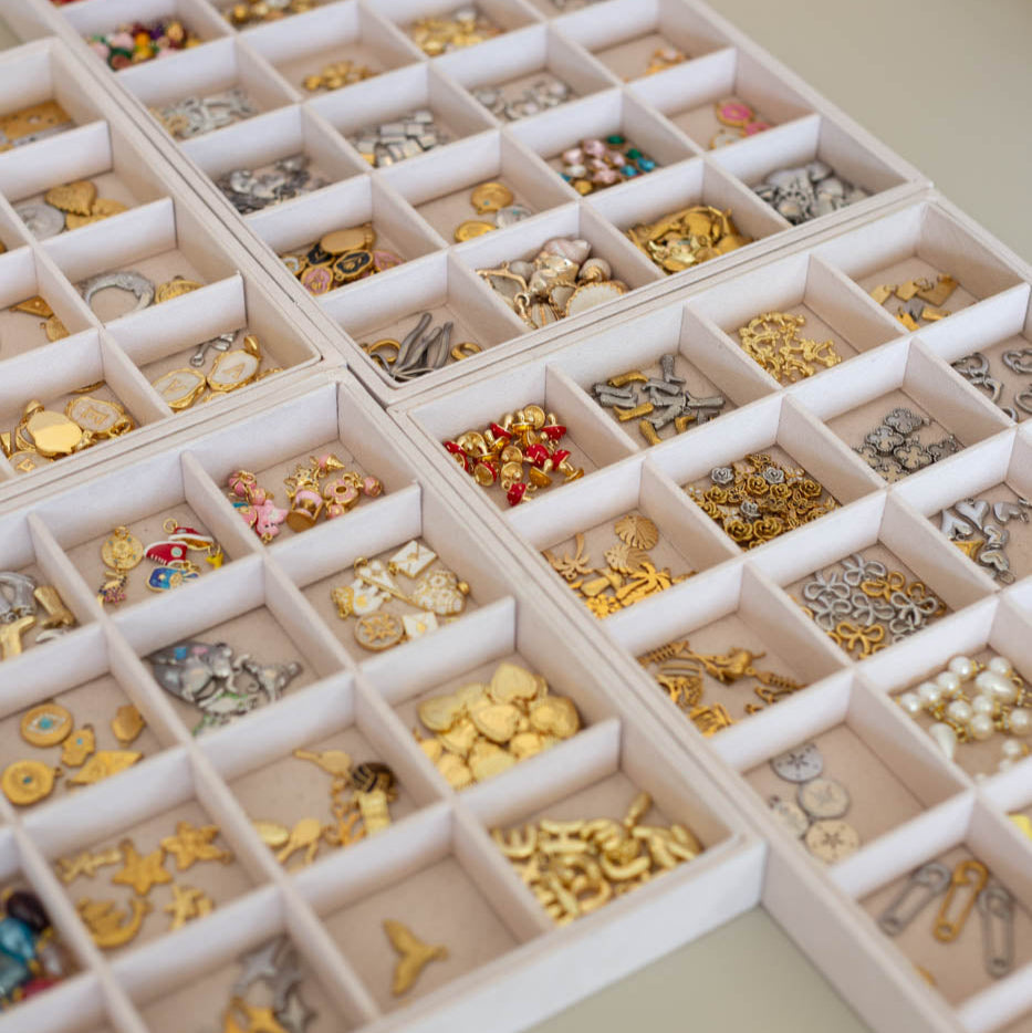 Assorted charms in a white organizer on a light coloured  velvet tray.